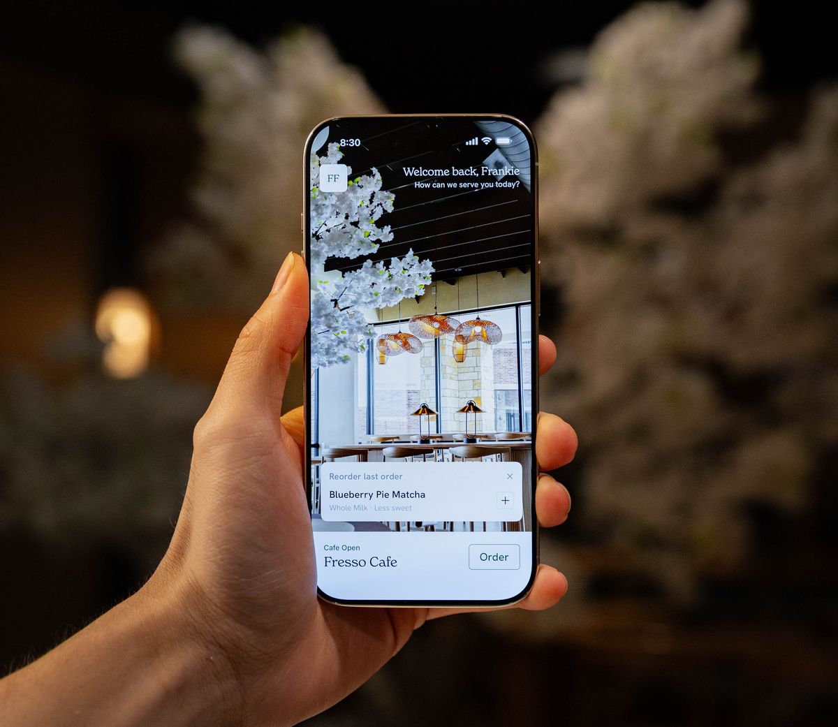 The Fresso Cafe app open on an iPhone, held up inside the cafe